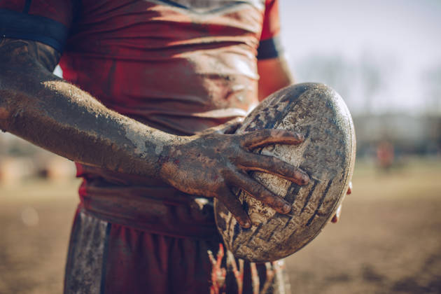 Man, vol met modder, houdt rugbybal vast tussen zijn handen