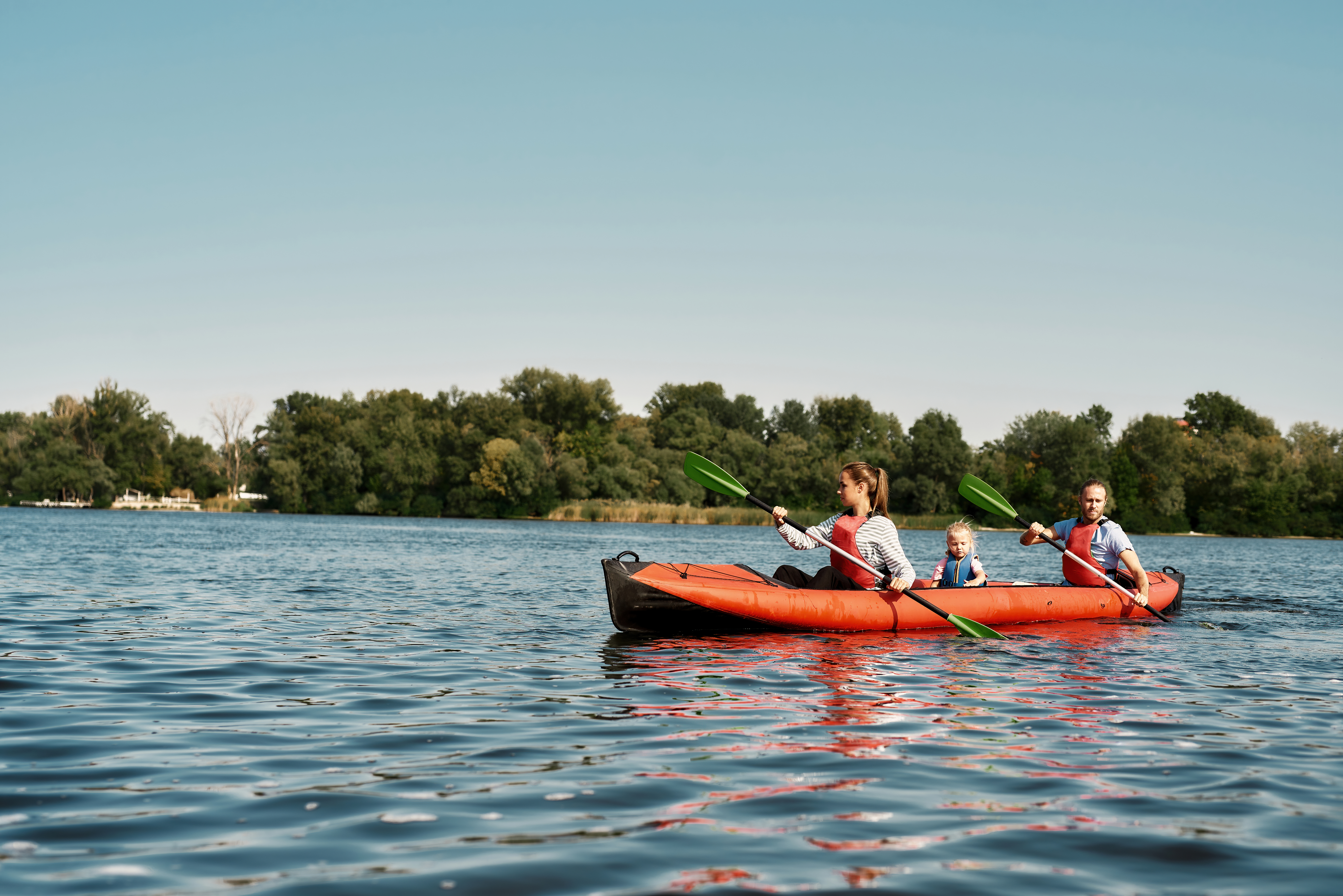Young caucasian family floating on kayak with paddles. Concept of rest, leisure and vacation at nature. Extreme water sport. Mother, father and daughter wearing life vests. Summer sunny daytime