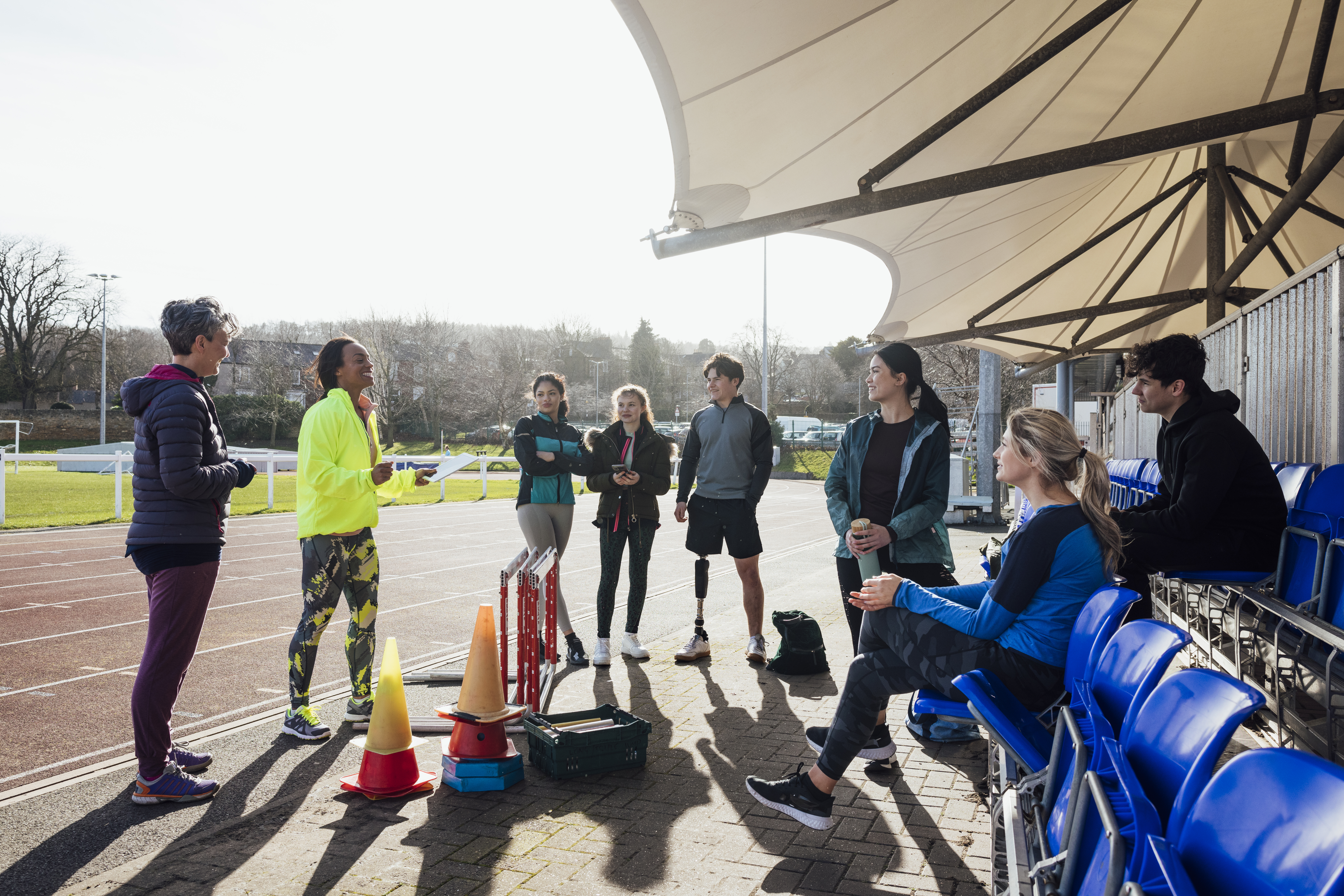 Groepje luistert naar trainer op piste, 1 man met beenprothese luistert mee