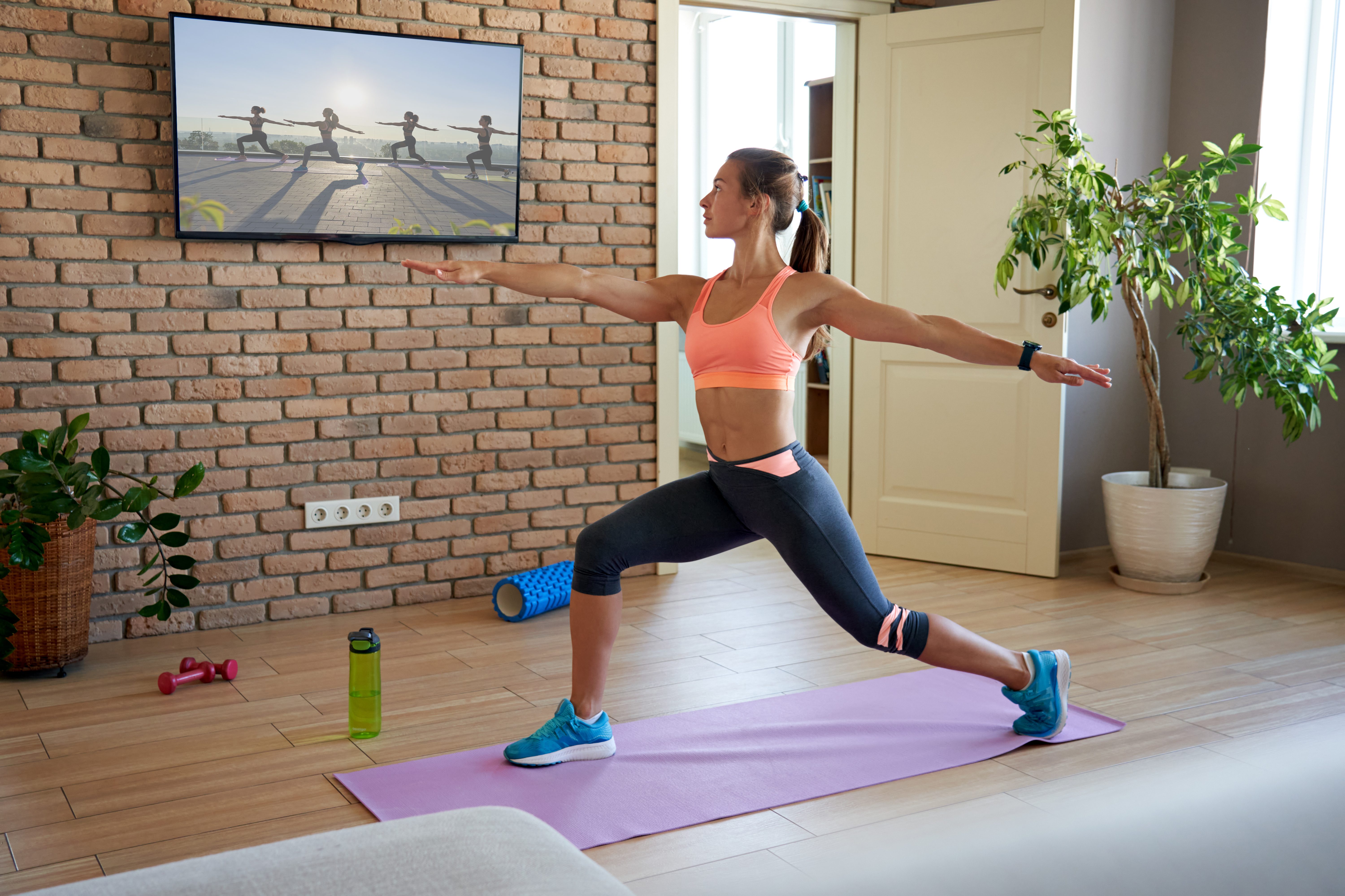 Fit sporty active young woman learning warrior yoga pose watching live streaming online workout exercise training weightloss class sport tv at home in living room. Fitness tutorialÂ  livestream concept