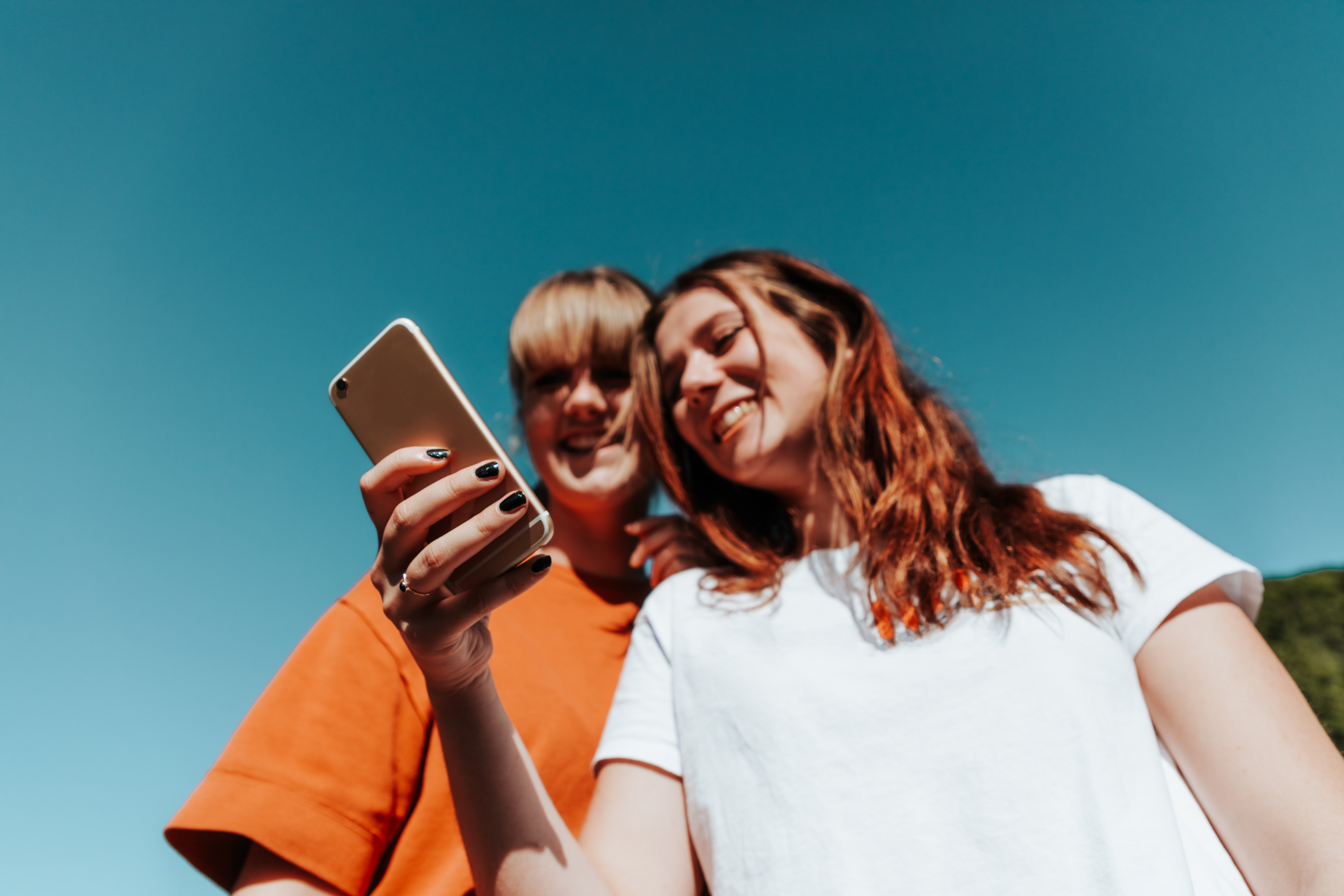 Happy smiling girls together having fun. Young female student friends reading text messages together on their Mobile Phone. Laughing and Smiling while reading the posts and watching funny video clips. Young Women Outdoor Lifestyle.