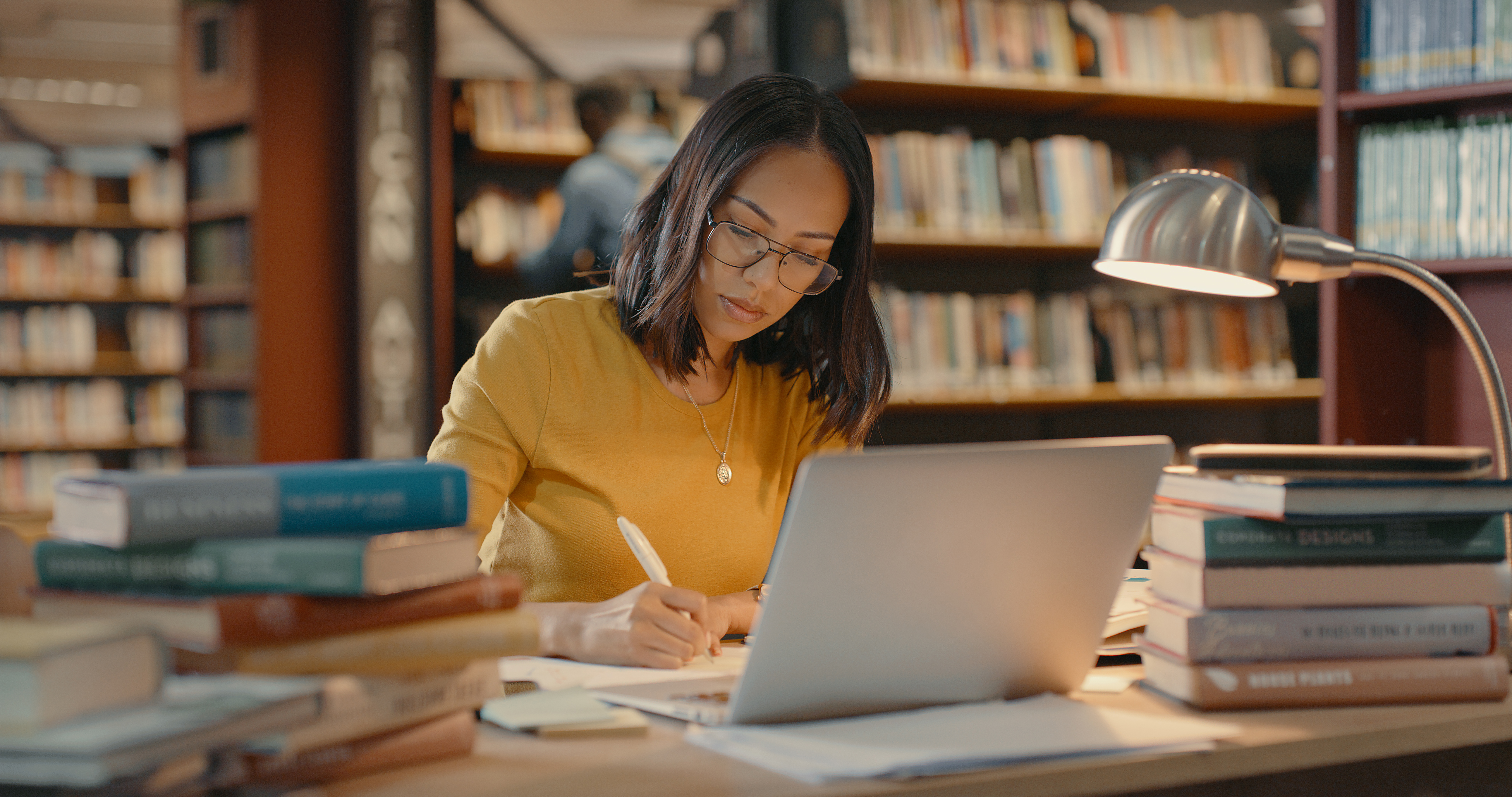 vrouw zit achter pc aan bureau met boeken opleiding leren