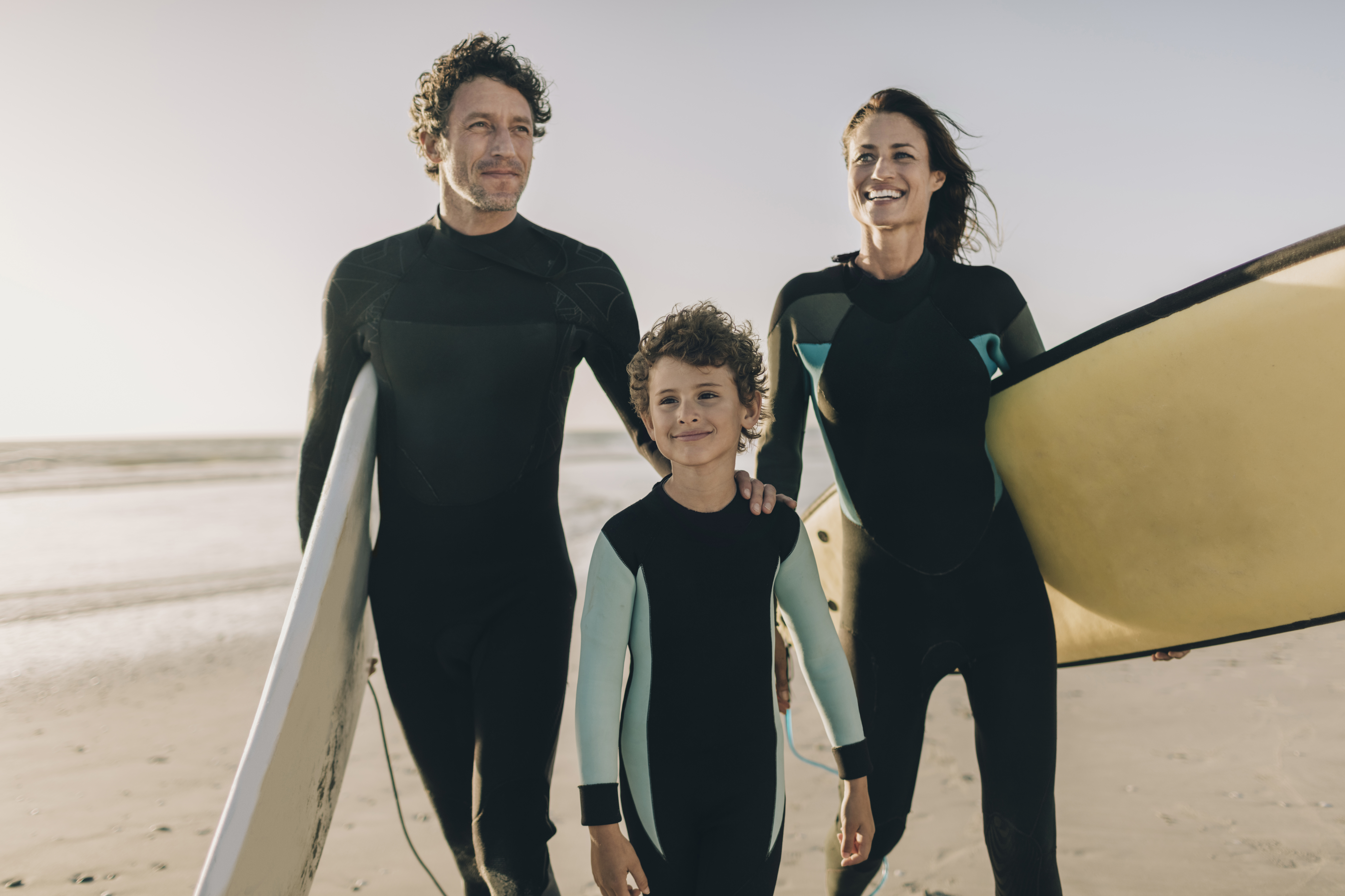 Close up of a family walking on the beach and carrying their surfboards