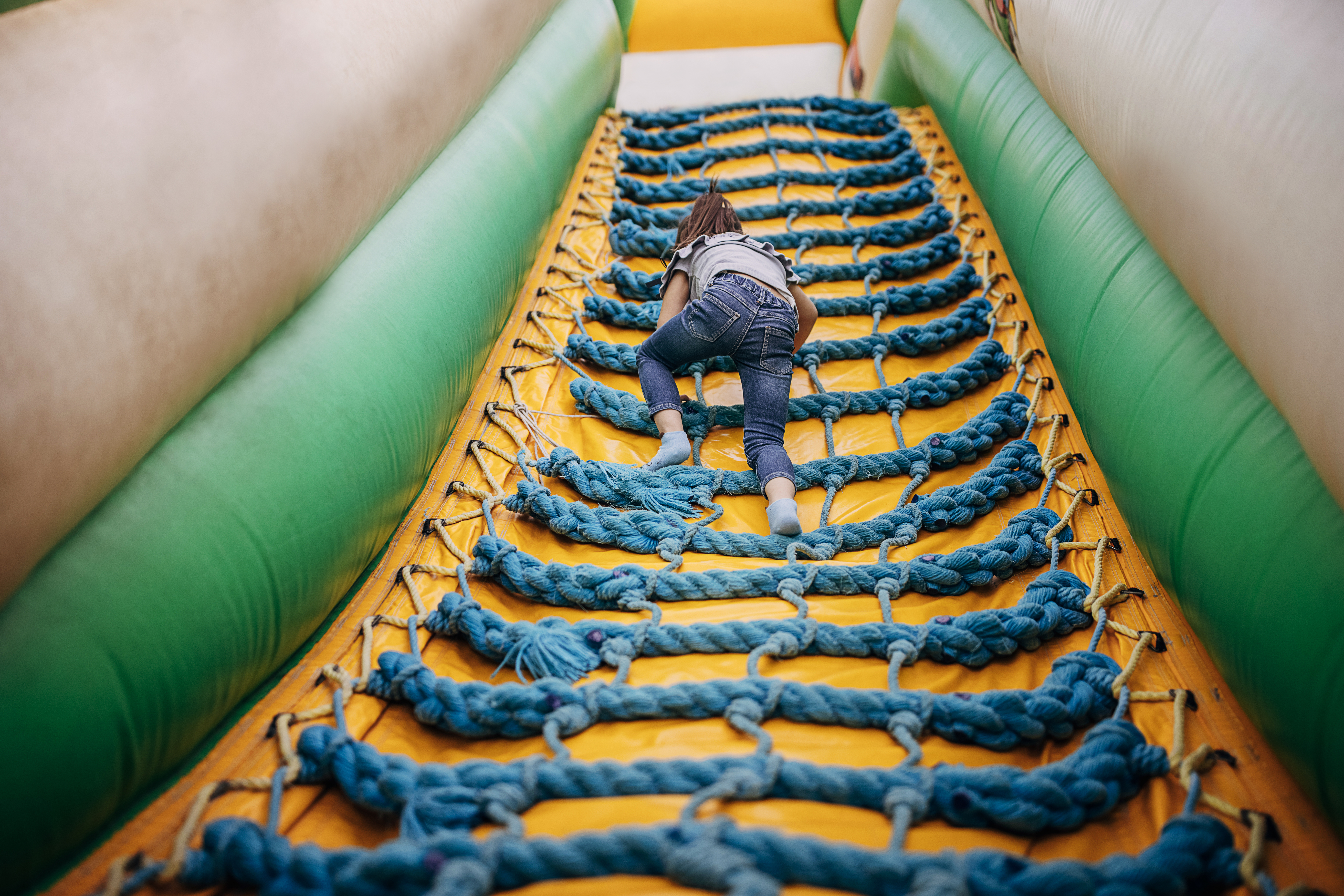 Cute little girl playing in climbing up inflatable bouncy castle in amusement park.