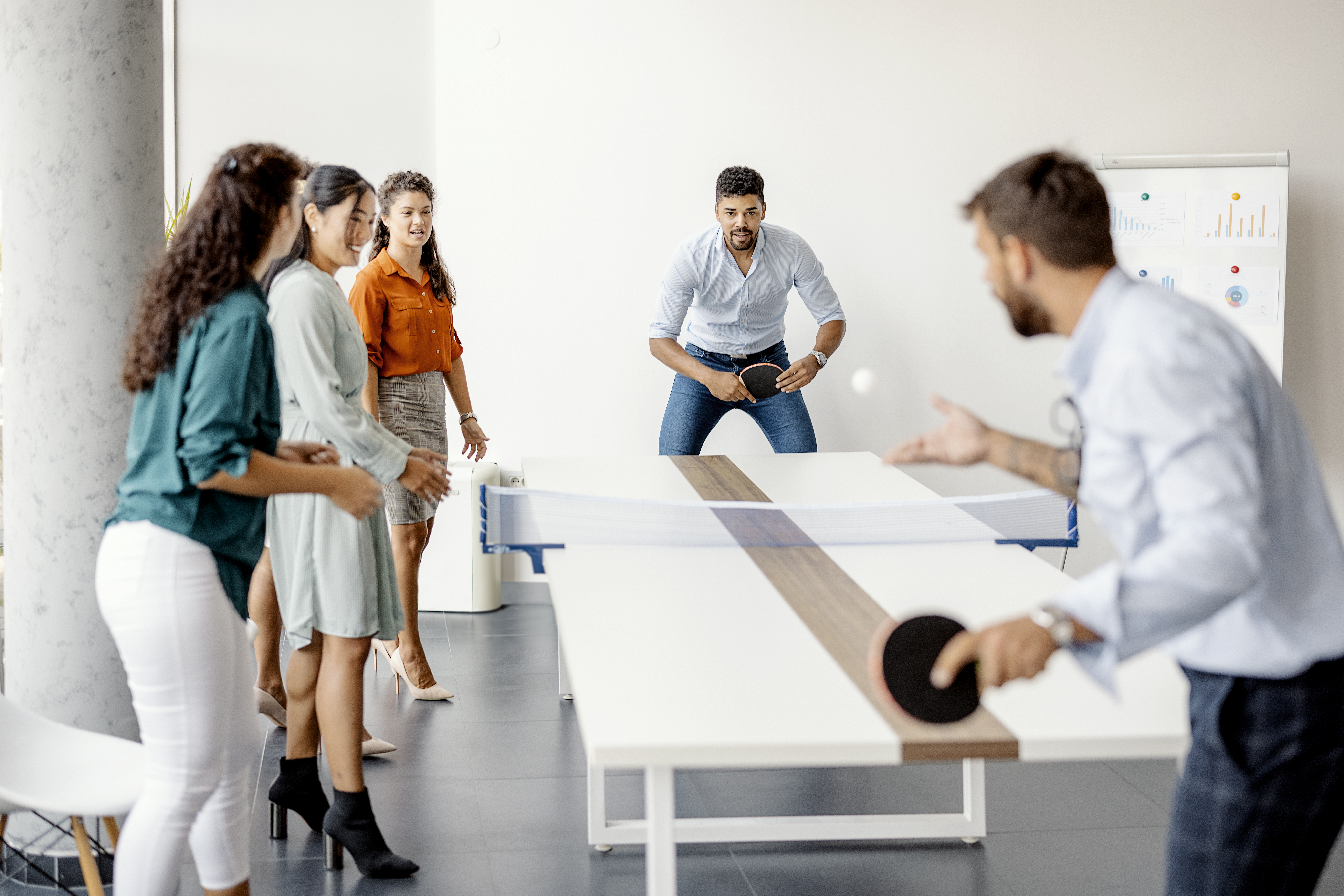 Group of young startup business people playing table tennis together on a boardroom table in an office while taking a break from their meeting