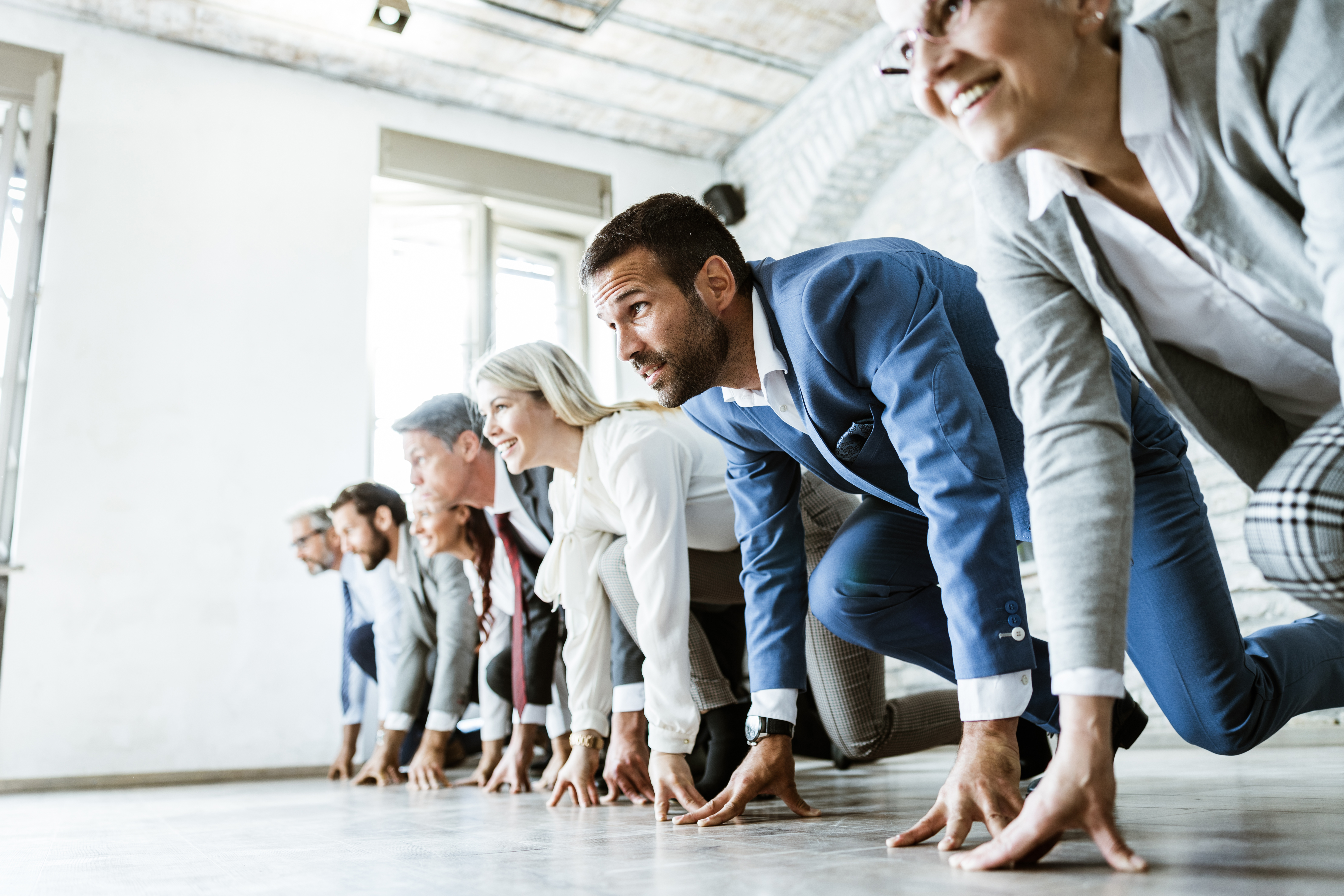 Large group of business people on a starting line ready for sports race in the office. Focus is on man in blue suit. Copy space.