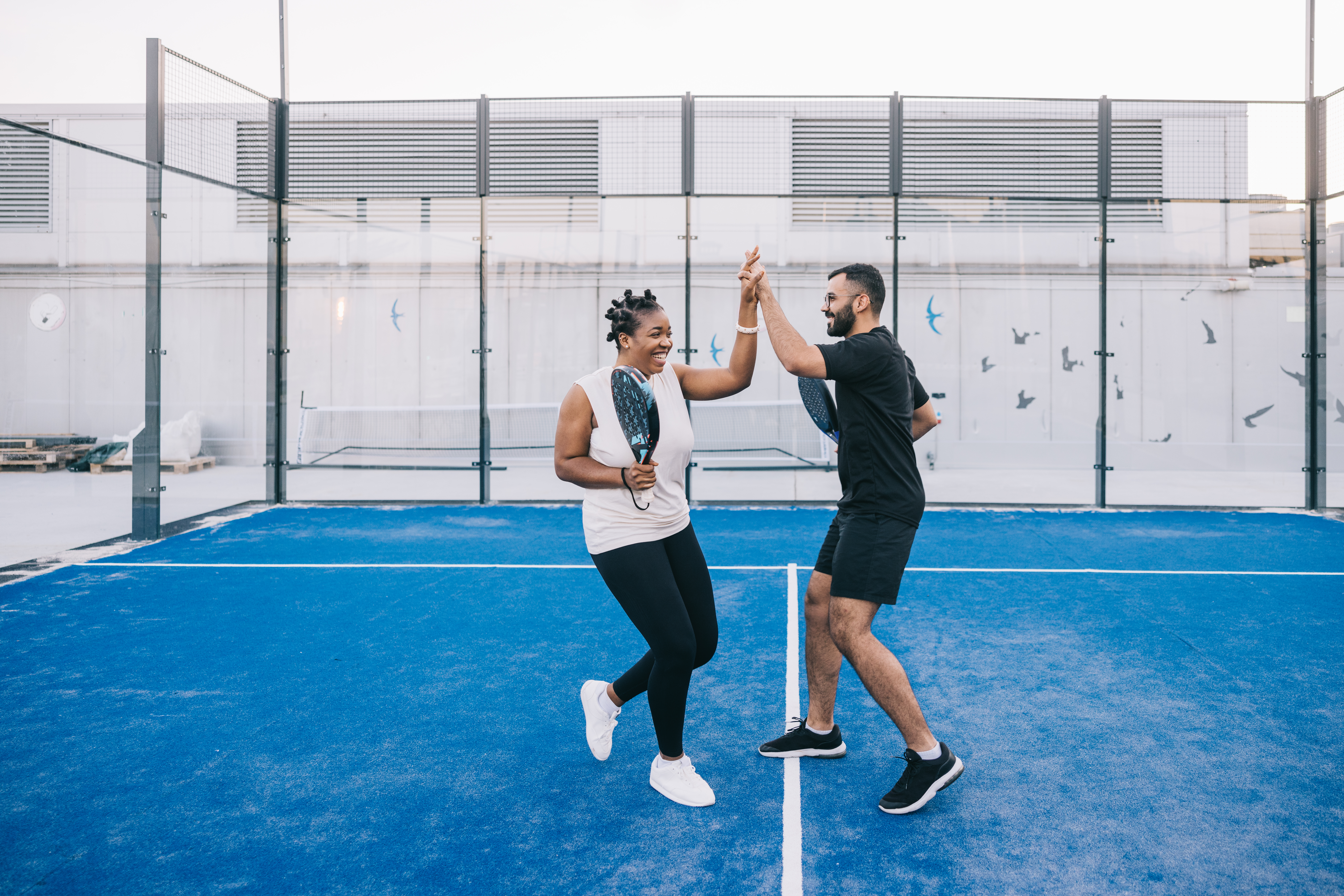 Een jonge vrouw en man geven elkaar high five bij spelletje padel