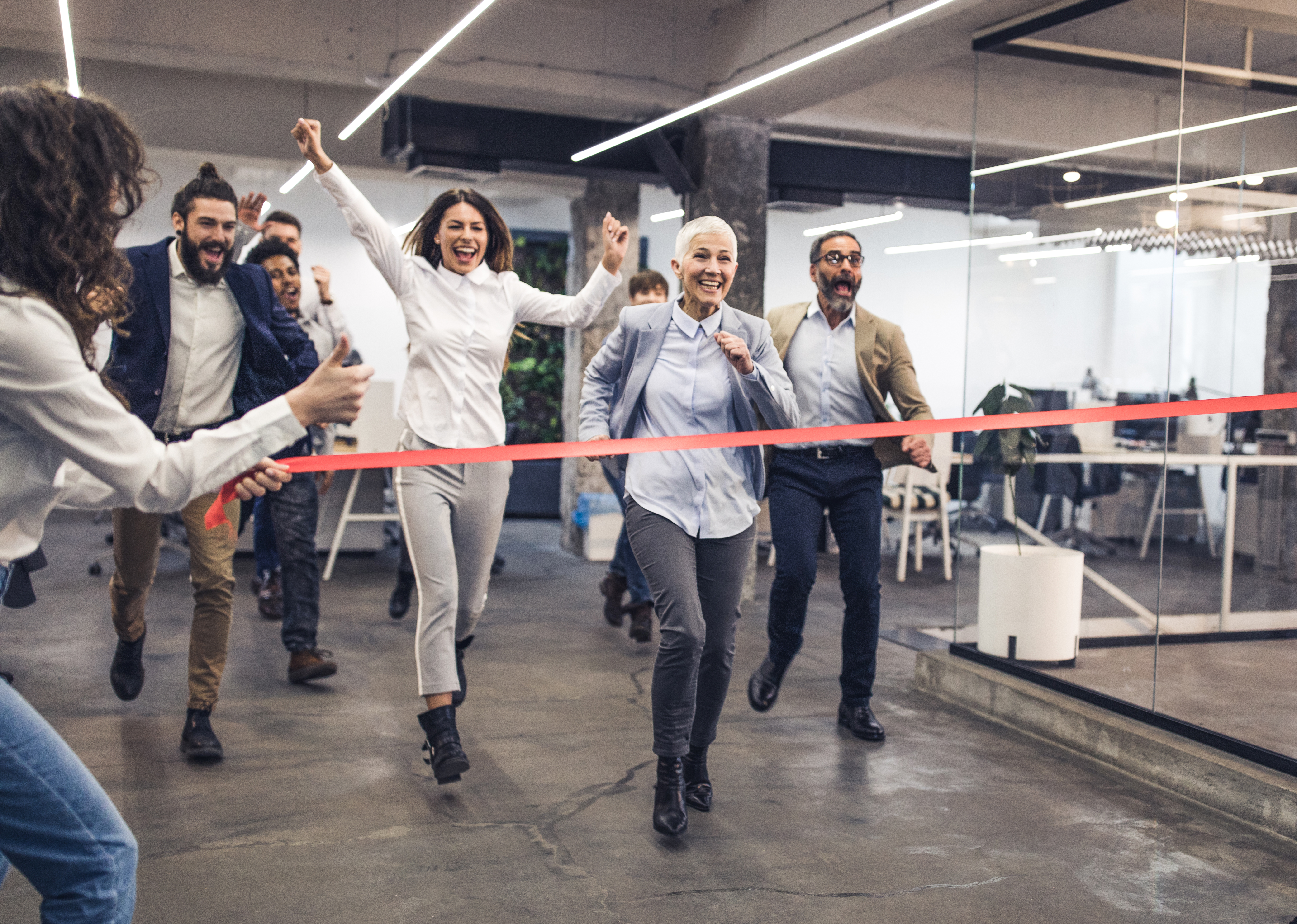Large group of happy business people having fun while having a race at casual office. Focus is on mature woman.