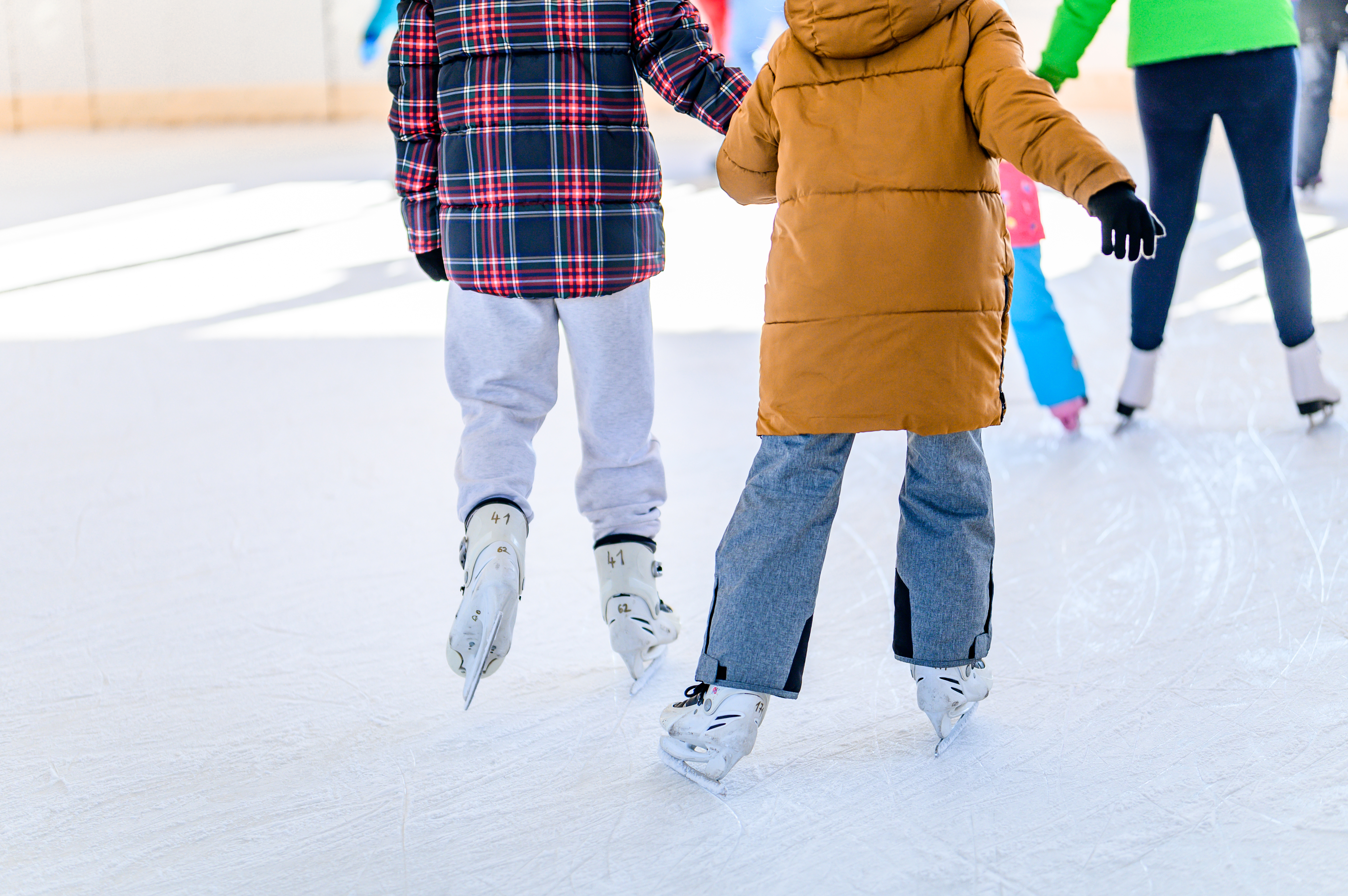 Two girls ice skating together and holding hands.