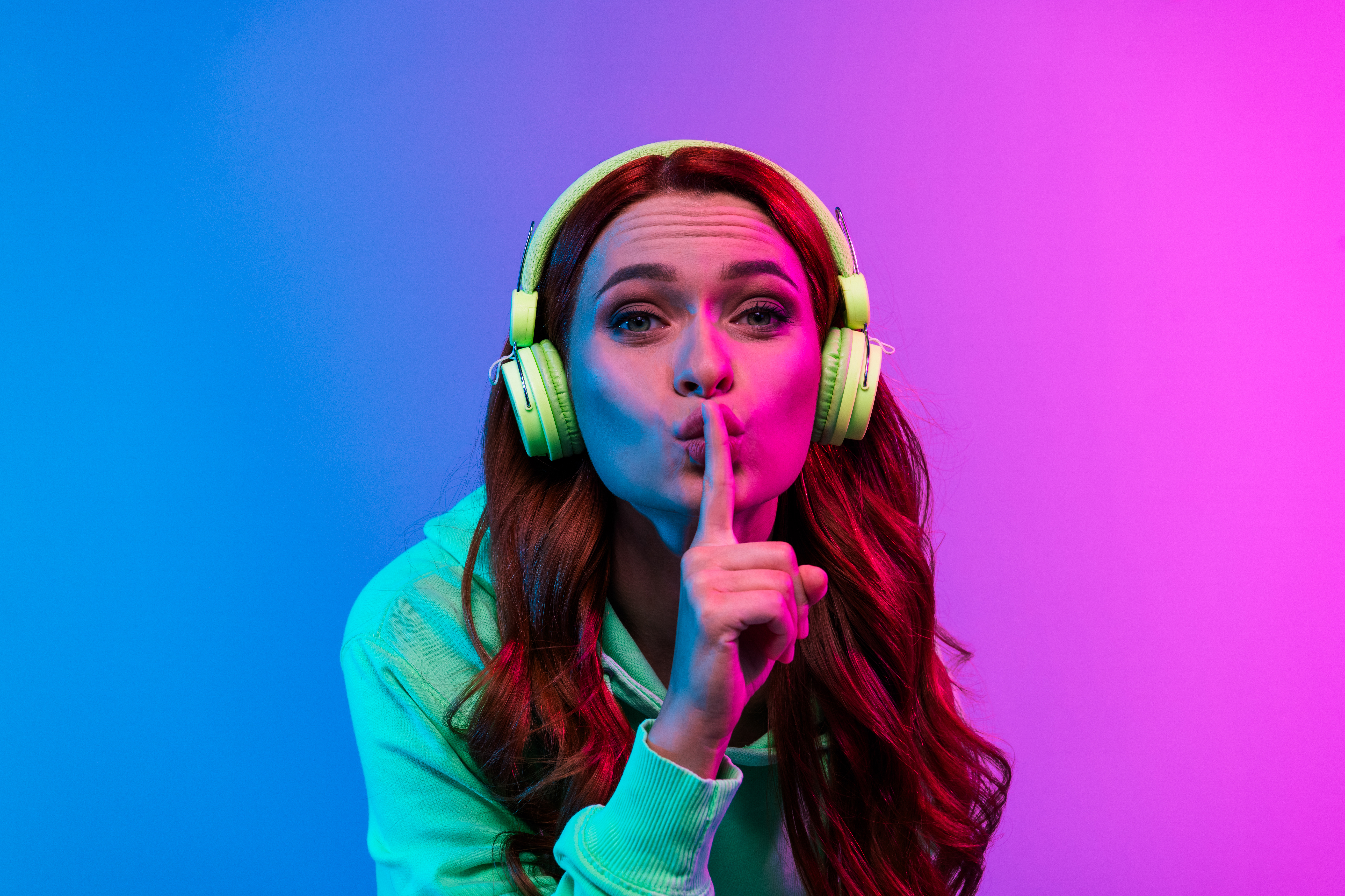 Photo of charming positive woman wear green sweatshirt headphones enjoy songs asking keep silence isolated neon blue color background.