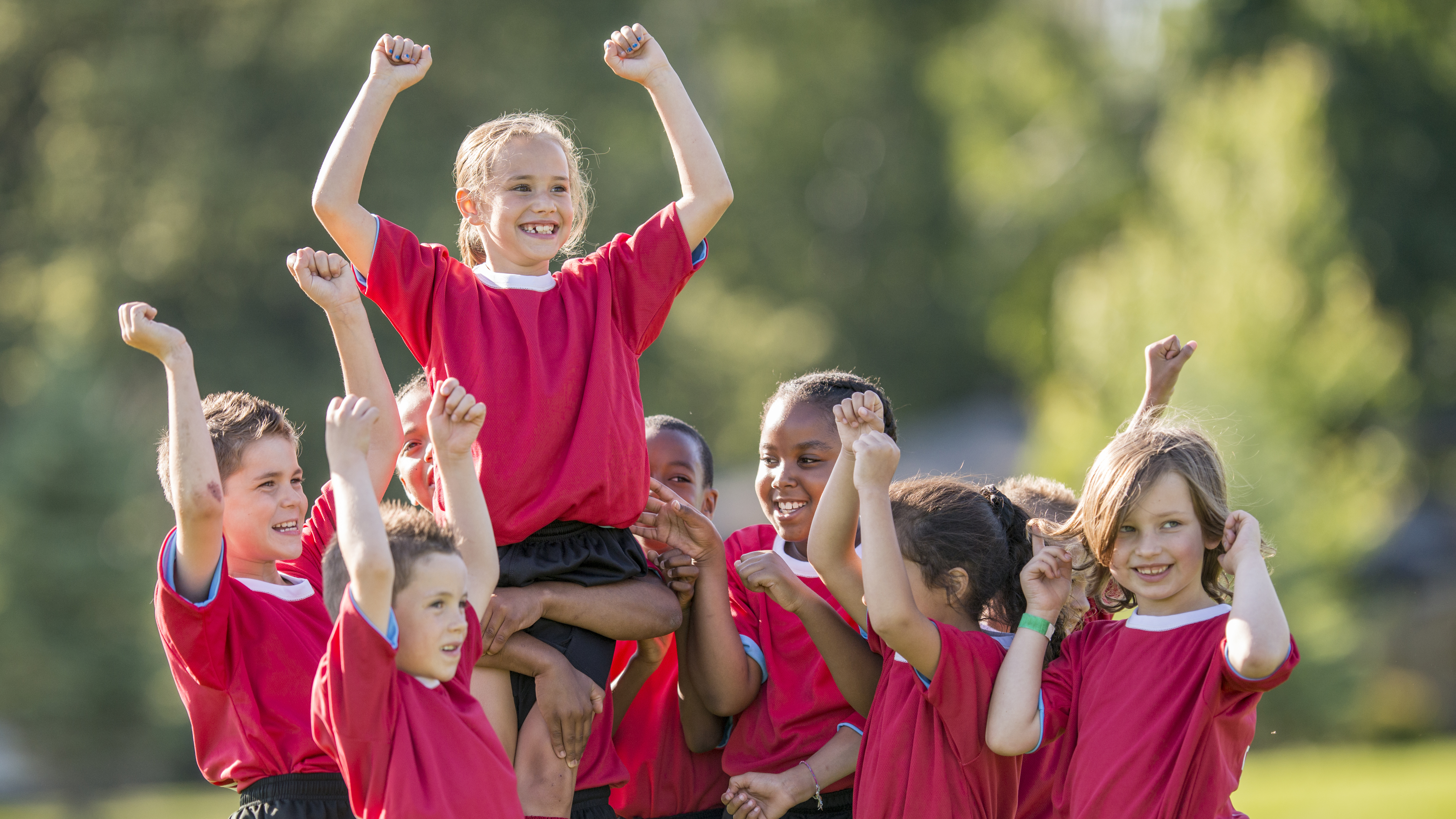 Multi culturele groep kinderen met handen in de lucht na doelpunt, één kind wordt omhooggestoken