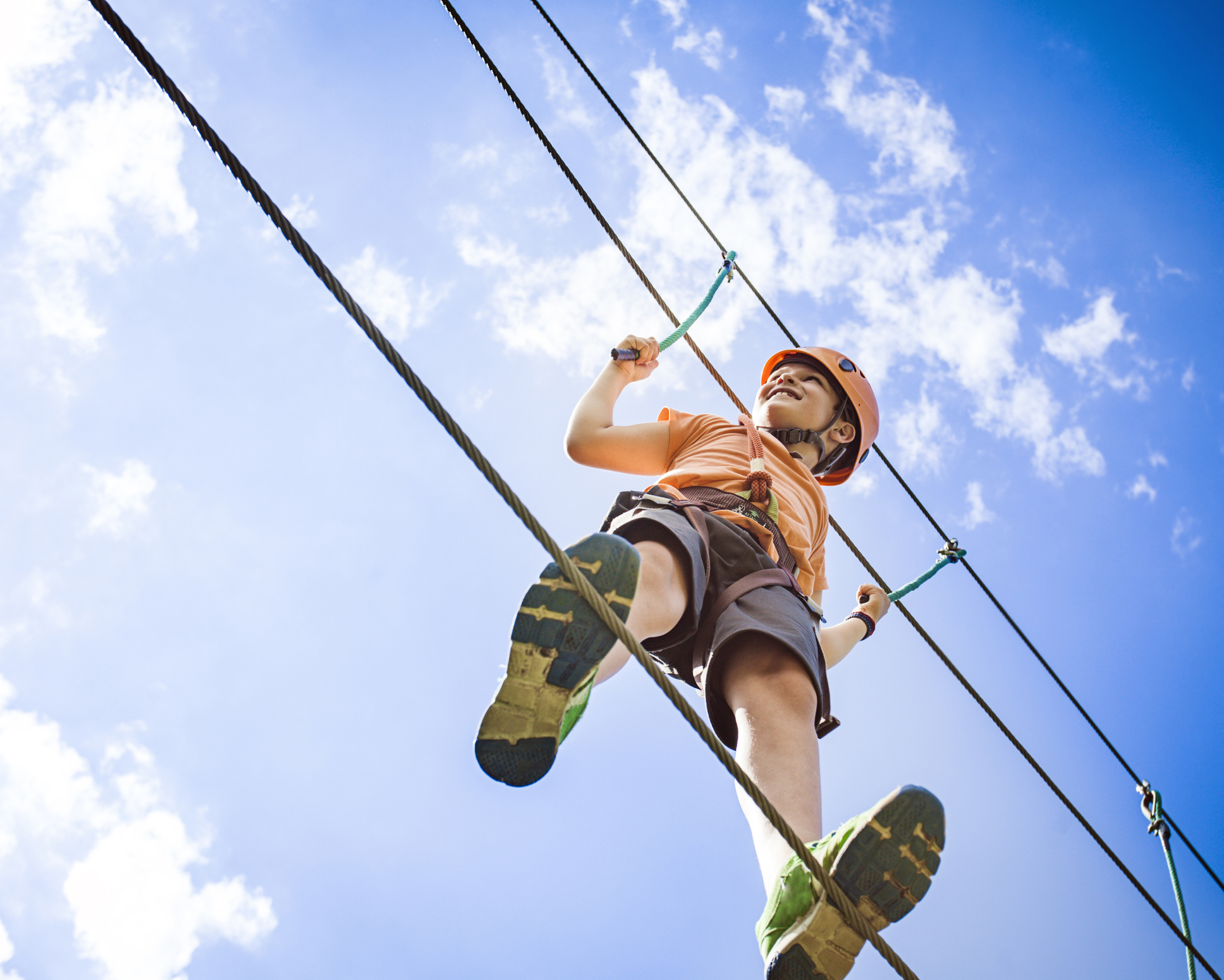 Boy at the adventure park walking on a rope high up in the air.