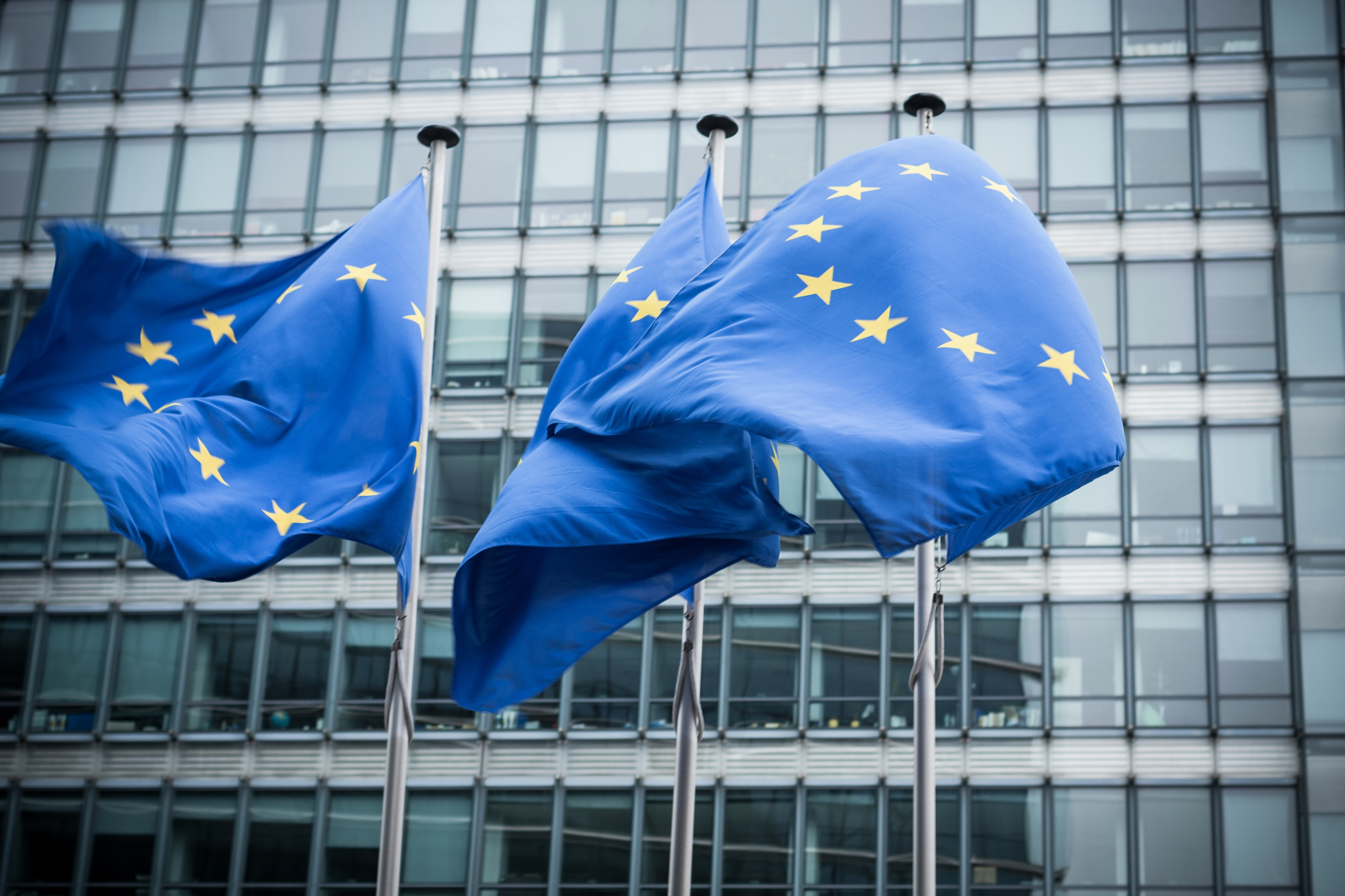 Drie Europese vlaggen wapperen voor het gebouw van de Europese Unie in Brussel