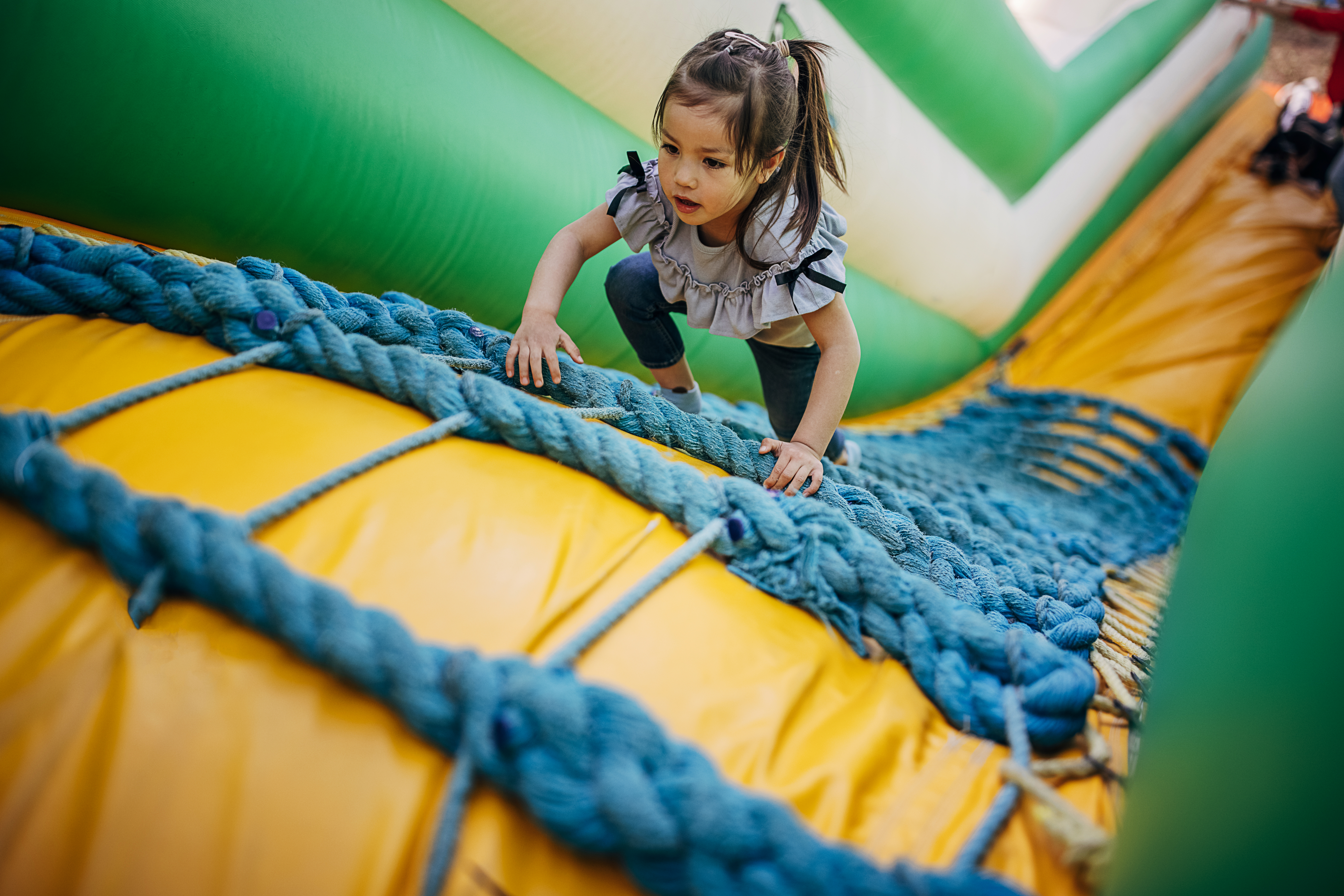 Cute little girl playing in climbing up inflatable bouncy castle in amusement park.