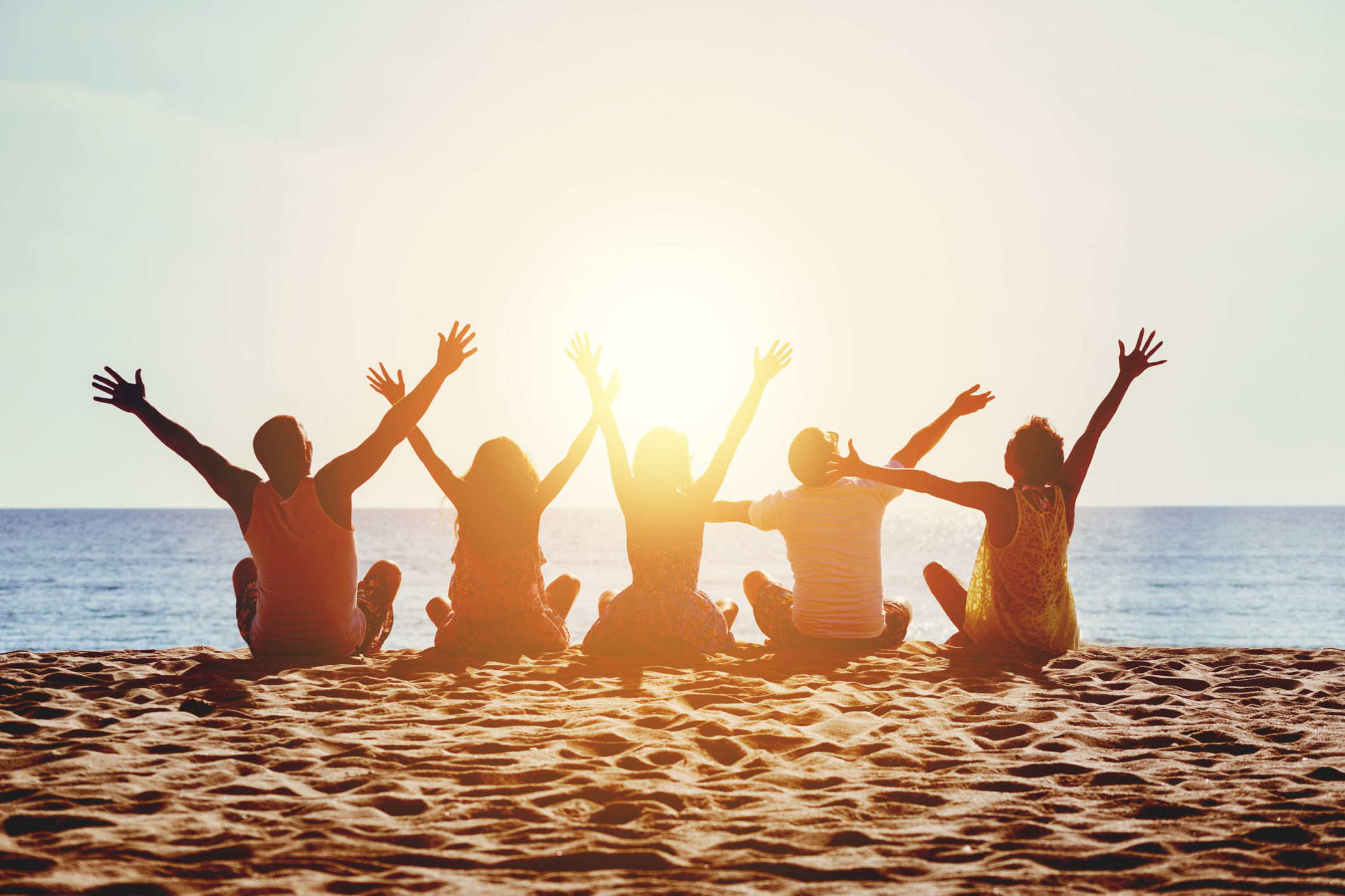Group of five happy people sits on background of empty sunset beach. Travel or sea vacations concept