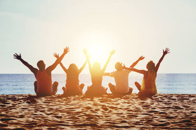 Group of five happy people sits on background of empty sunset beach. Travel or sea vacations concept