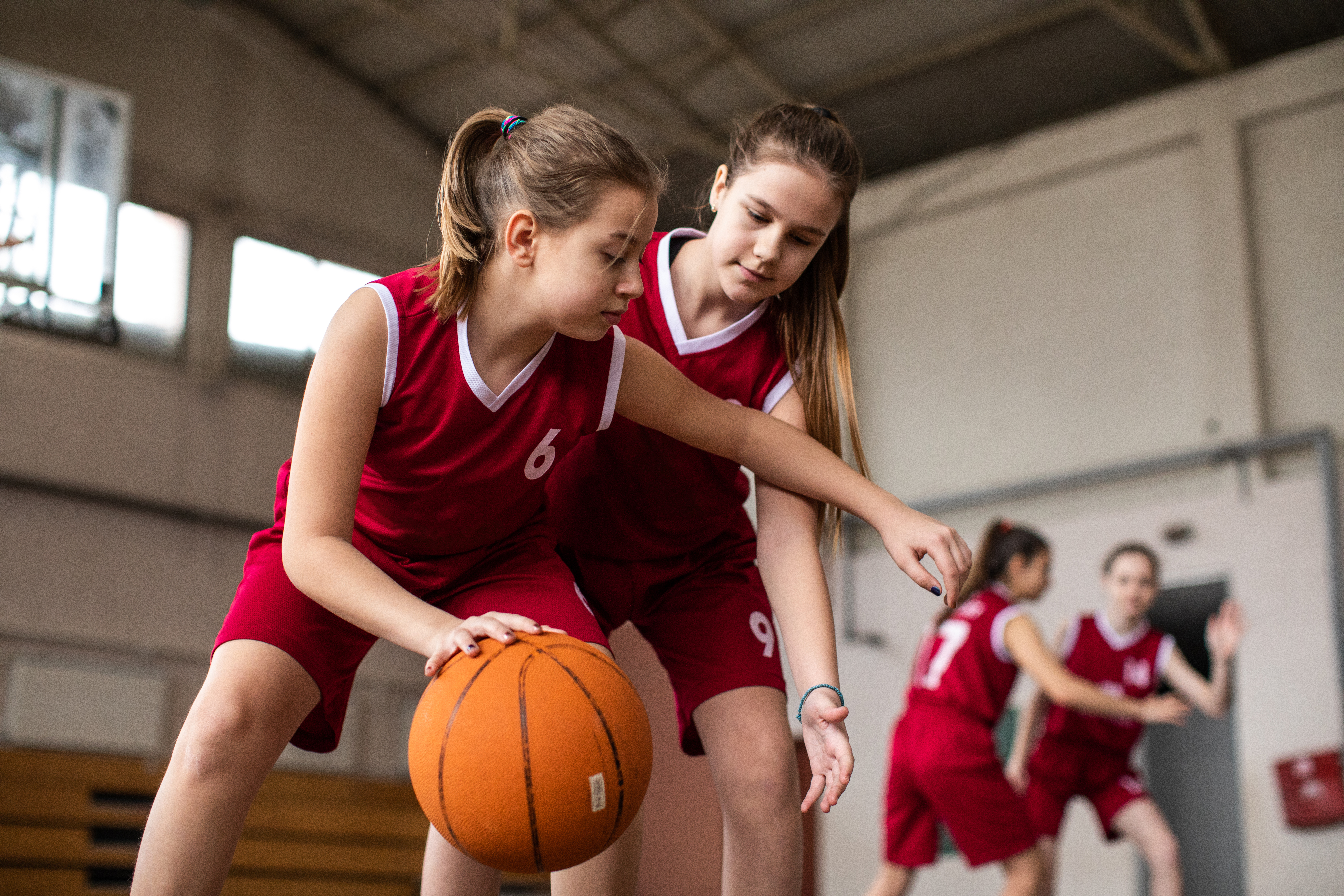 Female basketball team playing match in school gym, dribbling ball on sport filed