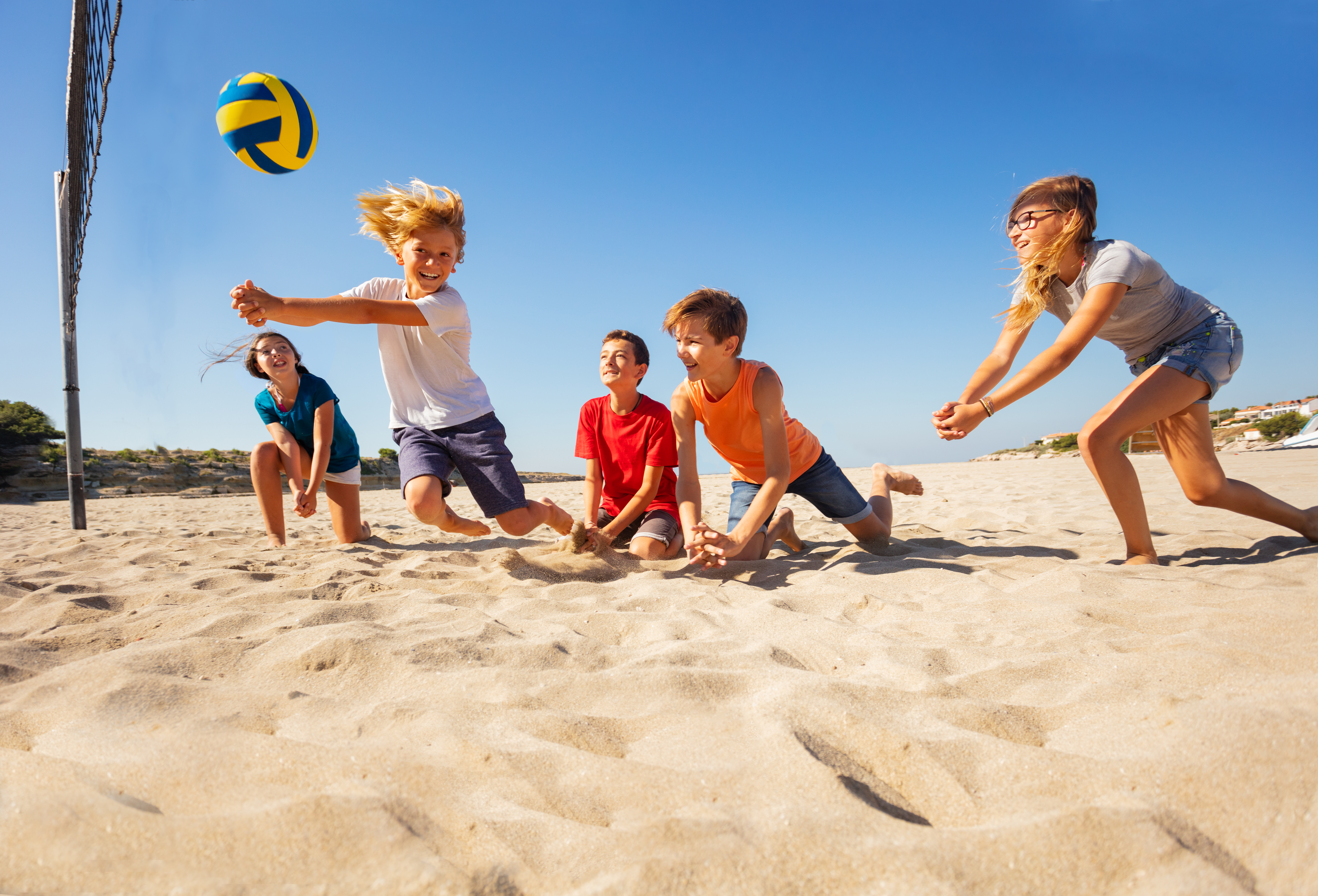 Groepje kinderen spelen volleybal op het strand, jongen slaat op